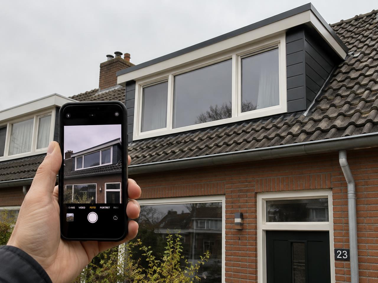 Iemand fotografeert een nieuw geplaatste dakkapel met een telefoon